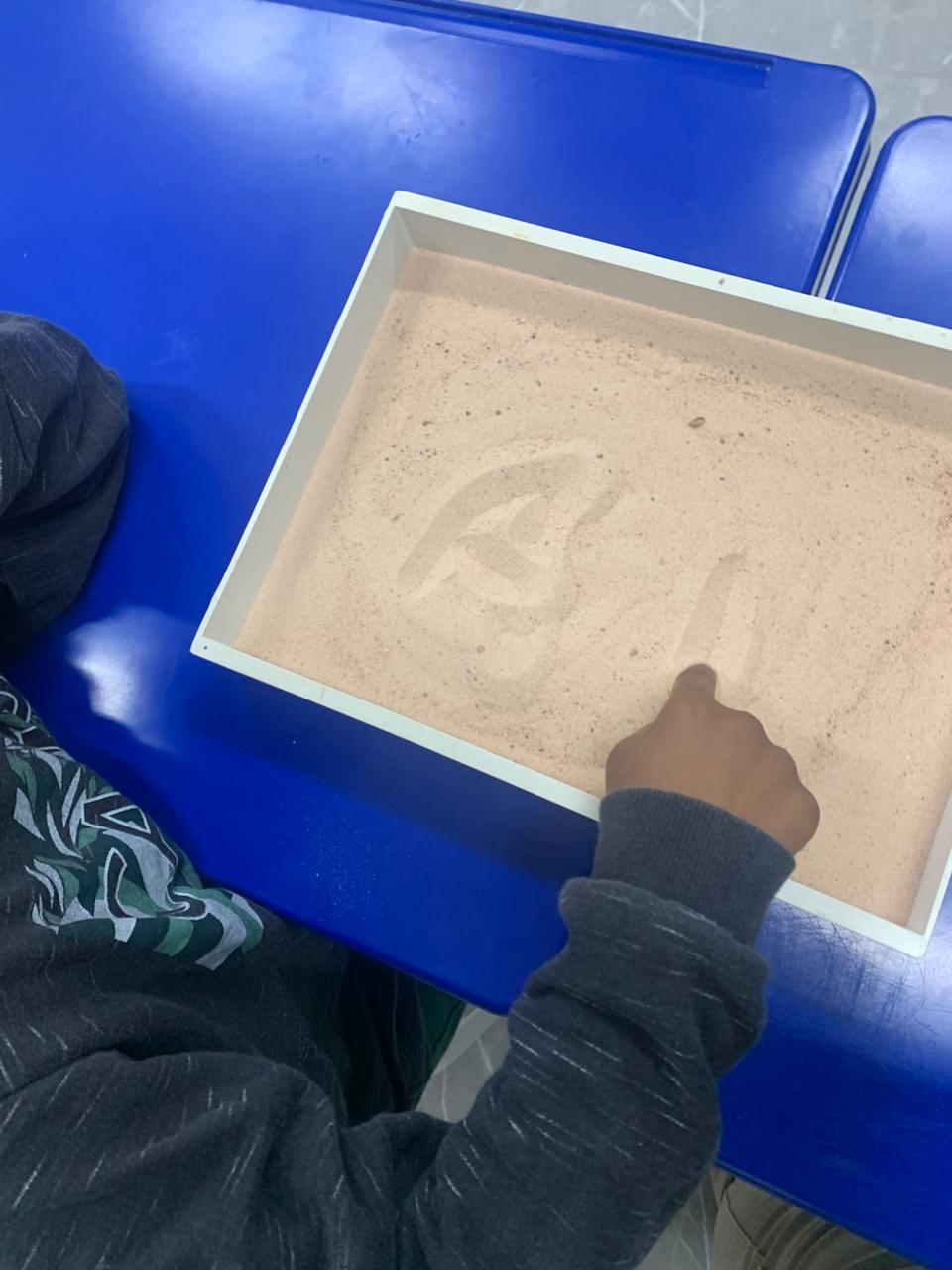 Criança escrevendo com o dedo em uma caixa de areia